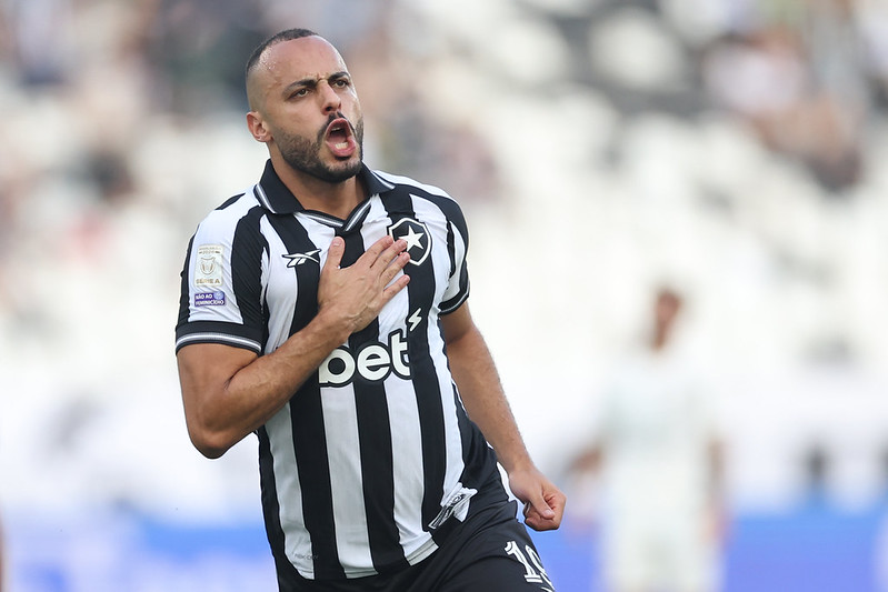 Arthur Cabral comemora gol pelo Botafogo com a mão no escudo da camisa.
